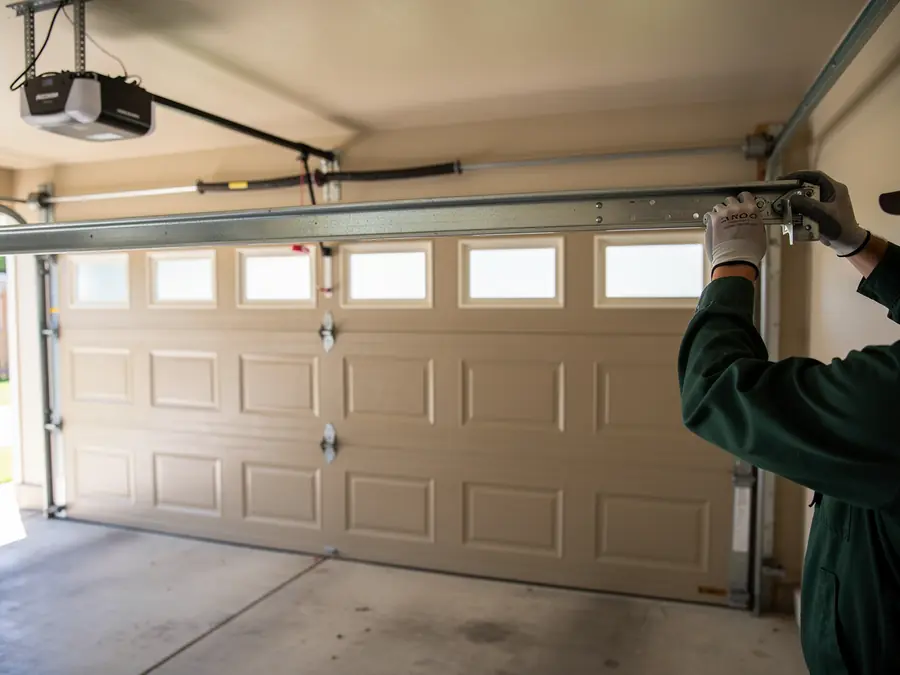 A technician in gloves is installing a garage door track above a closed garage door.