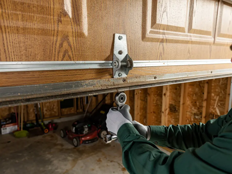 A technician adjusts a garage door roller with a wrench.